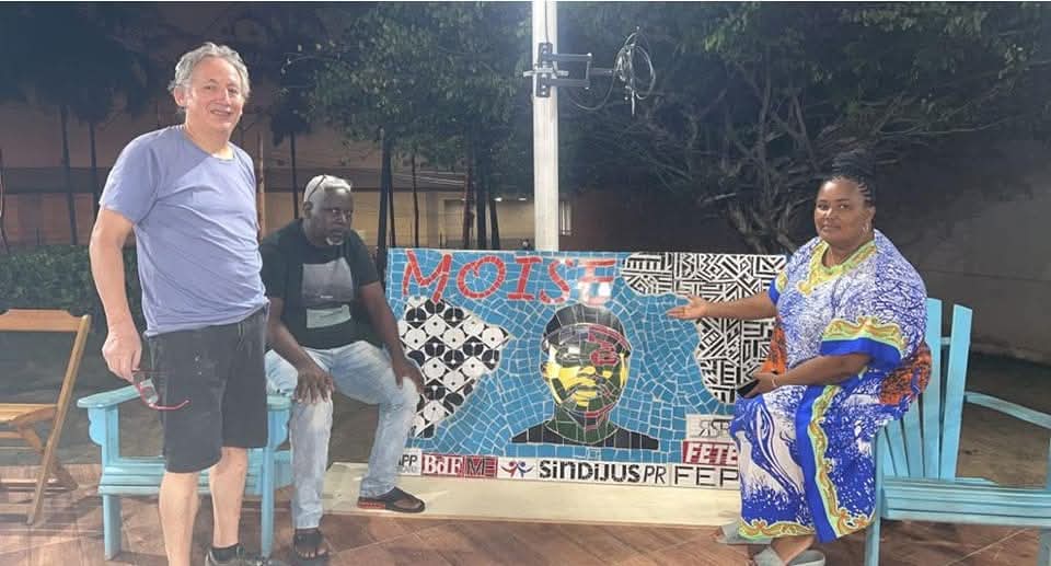 Javier Guerrero ao lado de um painel comunitario em mosaico, com participantes da atividade.